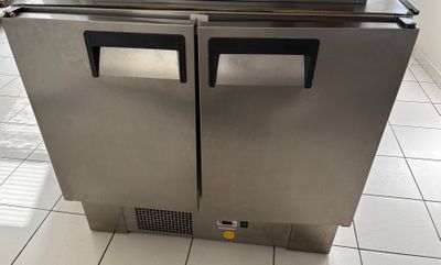 congélateur à double porte en acier inoxydable posé sur un sol carrelé dans une cuisine professionnelle