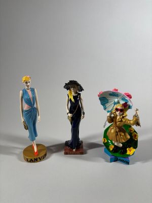 Trois figurines de styles et de couleurs différents sont exposées sur un fond blanc