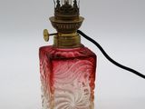 une image représentant un flacon de parfum en verre rouge et blanc surmonté d'une lampe