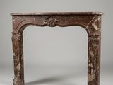 un encadrement de cheminée ancien en marbre, orné d'un motif sculpté sur le dessus
