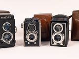 several old cameras are lined up in a row on a white surface