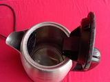 a silver coffee pot with a black handle on a red table