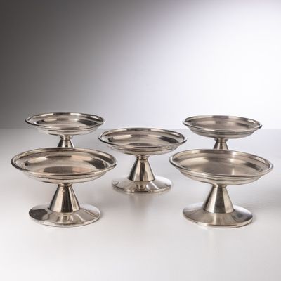 six plats plaqués argent posés sur des socles, disposés sur un fond blanc