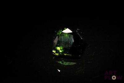 un gros plan d'une tourmaline verte posée sur une surface noire