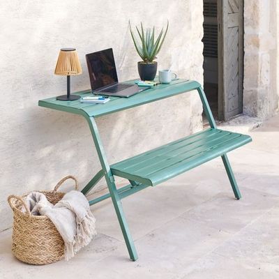 un ordinateur portable posé sur un banc vert à côté d'un panier