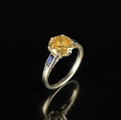 une bague sertie d'un saphir jaune et de diamants, posée sur un fond noir
