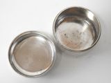 two small metal bowls sitting on a white surface