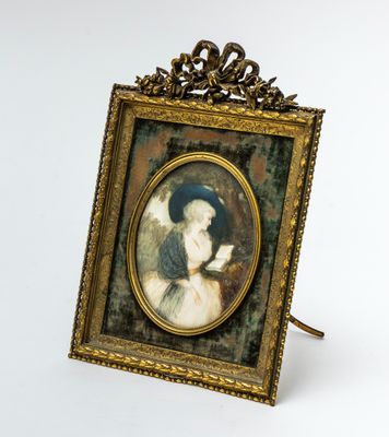 an old picture of a woman in a blue hat is hanging on a gold frame