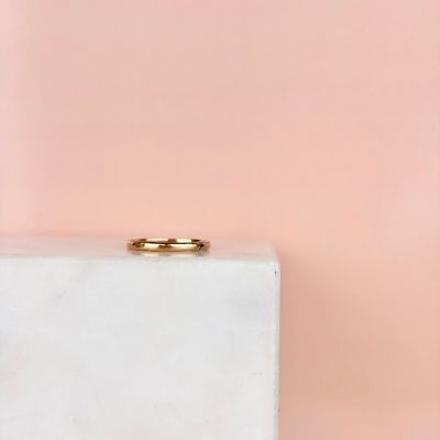 une alliance en or posée sur un bloc de marbre blanc, sur fond rose