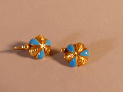 une paire de boucles d'oreilles en forme de fleurs aux teintes bleues et dorées sur un fond beige