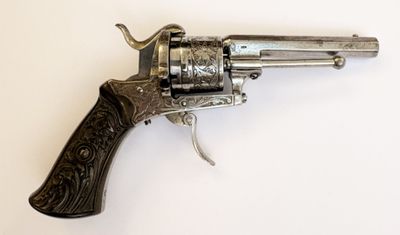 un vieux revolver en argent avec une crosse en bois, posé sur une surface blanche