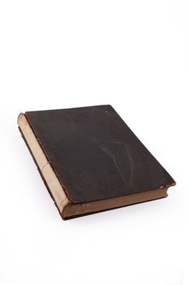 an old book with a black cover sitting on a white surface