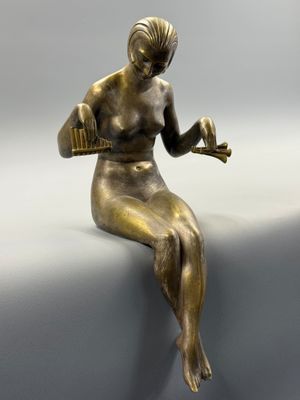 statue en bronze représentant une femme assise sur un rebord, tenant un oiseau dans ses mains