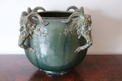 a green vase with two rams on it sitting on a table