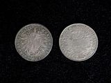 two silver coins sitting side by side on a black surface