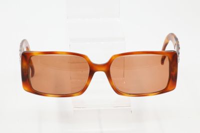 des lunettes de soleil marron posées sur un support transparent, sur une surface blanche