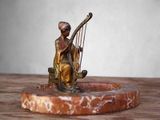 une statue représentant une femme jouant de la harpe, posée sur un socle en marbre