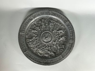 une plaque d'argent ornée d'un motif sur une surface blanche