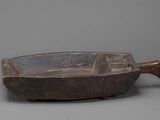 an old wooden bowl with a handle on a gray surface