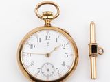 a gold pocket watch and a gold tie bar on a white surface