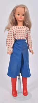 une poupée aux cheveux blonds, portant un pantalon bleu et des bottes rouges
