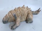 une petite statue représentant un dinosaure posée sur une surface blanche
