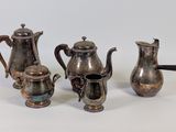 three silver teapots and a coffee pot on a white surface