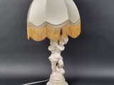 a white table lamp with a white shade and gold fringes on it