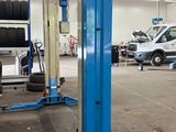 un pont élévateur bleu dans un garage, avec d'autres voitures en arrière-plan