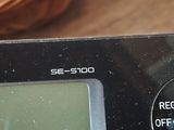 a digital clock on a table with a basket of candy in the background
