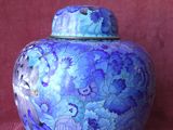 un vase violet et bleu posé sur un tissu rouge, sur fond rouge