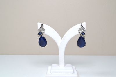 une paire de boucles d'oreilles en verre bleu et argent, posée sur un socle blanc