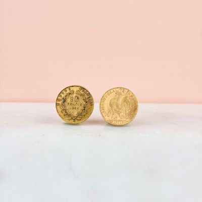 a pair of gold coin stud earrings sitting on top of a marble counter