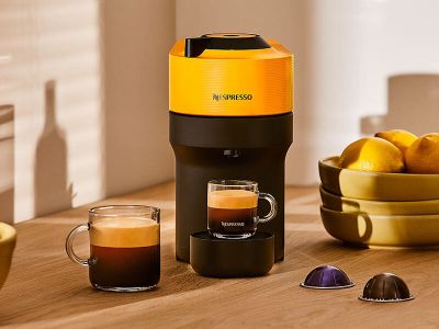 une cafetière posée sur une table, à côté d'un bol de fruits et d'une tasse de café