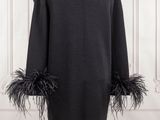 the back view of a black coat with feathers on a mannequin