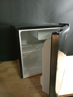 un petit réfrigérateur dont la porte est ouverte, posé sur un plancher en bois