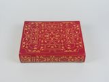 une boîte rouge ornée de motifs dorés, posée sur une surface blanche