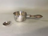 une tasse en argent avec une cuillère et un repose-cuillère posés sur une table
