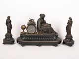 trois statues et une horloge posées sur une table