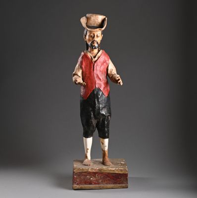 statue d'un homme vêtu d'un gilet rouge et d'un chapeau, debout sur un bloc de bois