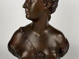 un buste en bronze représentant une femme en robe, posé sur un socle