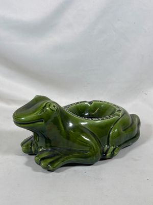 une grenouille en céramique verte posée sur un tissu blanc