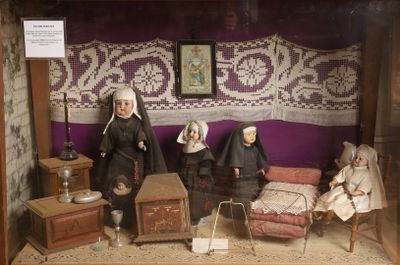 Les poupées sont exposées dans une vitrine, avec un mur violet en arrière-plan.