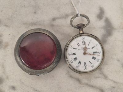 une montre de poche en argent et une montre en verre rouge posées sur une surface en marbre