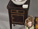 a small doll sitting next to a small table with a bowl on top of it
