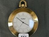 a gold pocket watch with a white face on a table