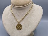 a gold necklace on a mannequin with a coin on it