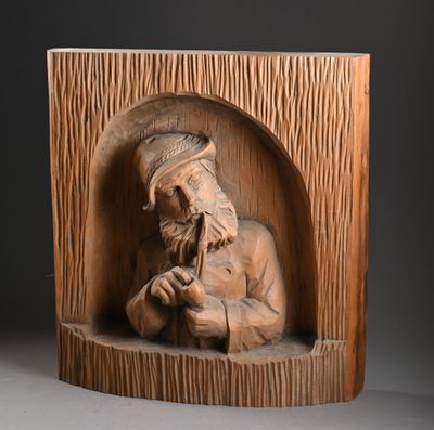 sculpture représentant un vieil homme barbu, coiffé d'un chapeau, assis dans une caisse en bois
