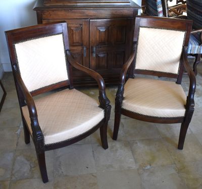 two wooden chairs with beige upholstered cushions sit in front of a dresser