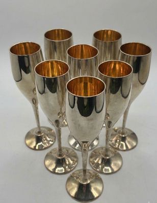 six silver wine goblets are lined up on a white surface